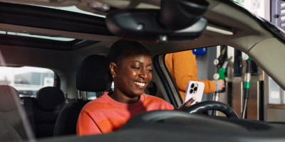 Woman sitting in car at fuel station using the Q8 app on her smartphone