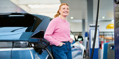 Femme se tenant à coté d'une voiture qui charge a la borne Q8 electric