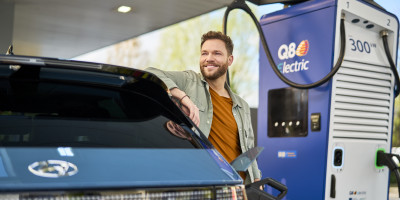 Un homme se tient à côté de l'Alpitronic HYC400 (400 kW DC) avec le branding Q8 electric pour charger sa voiture.