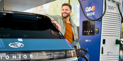 Un homme se tient à côté de sa voiture en train de se recharger, à côté d'une borne de recharge Q8 electric.